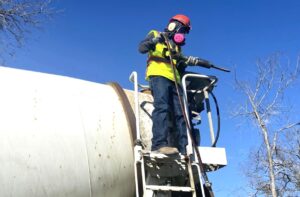 General Chipping employee in PPE holding a handheld pneumatic jackhammer on a ladder in front of a ready mix truck